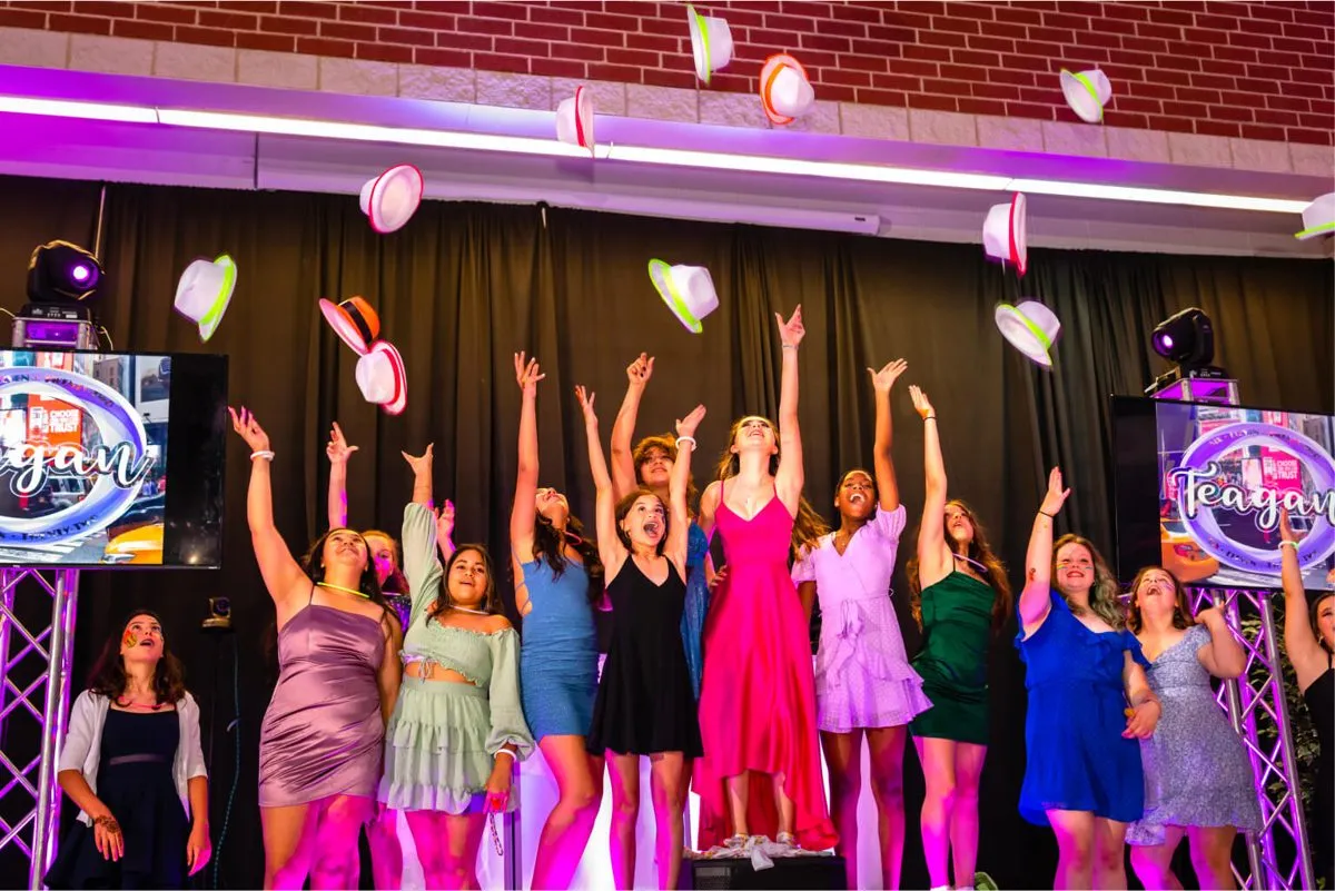 Teens tossing colorful party hats in the air on the dance floor at a bat mitzvah.