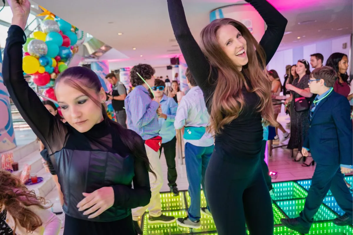 Group of teens dancing under colored lights at a mitzvah party.