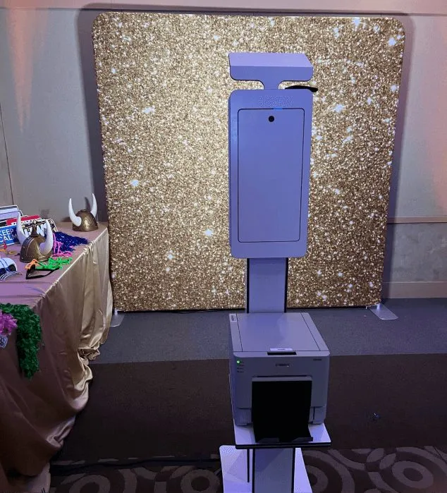 Open-air print photo booth kiosk set up beside a backdrop, ready for guests.