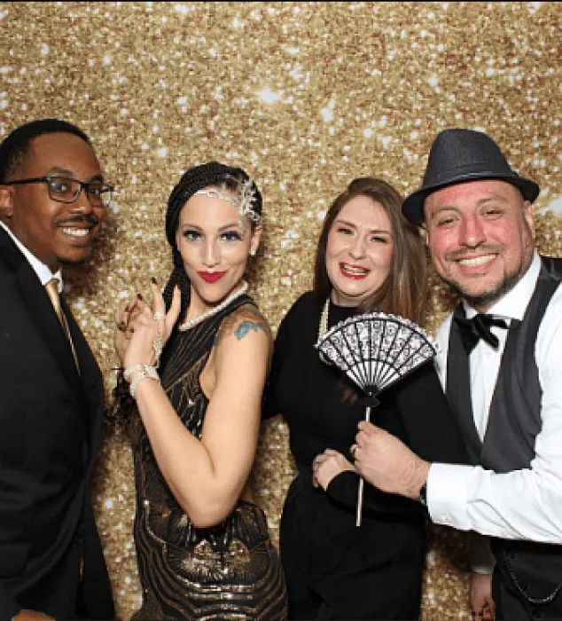 Four guests at a themed party holding photo booth props and smiling for the camera.