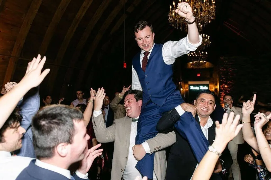 Wedding DJ mixing behind a lit facade booth while guests dance in front of him.